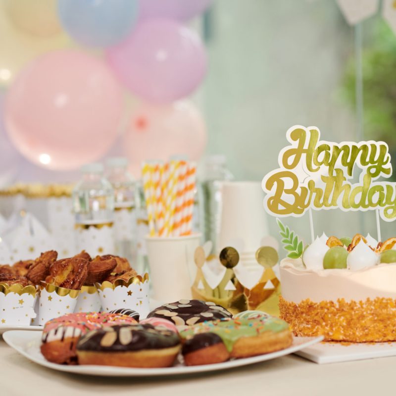 Decorated birthday cake, doughnuts and cupcakes on table prepared for party guests